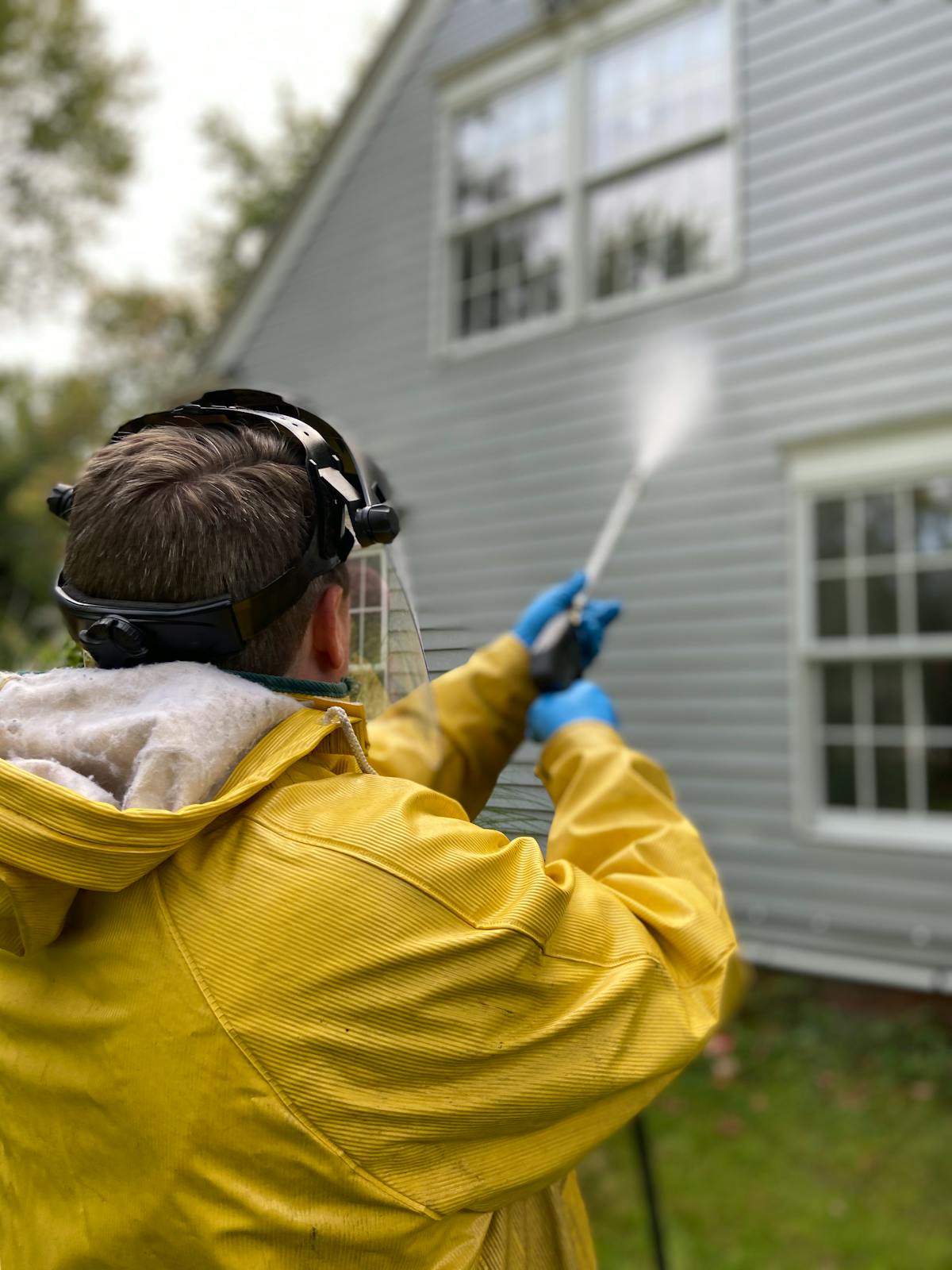 Technician in yellow rain gear pressure washing home exterior siding