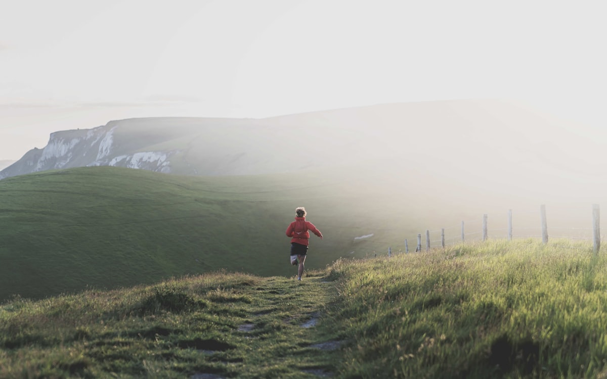 A runner moving along a grassy hillside trail at sunrise