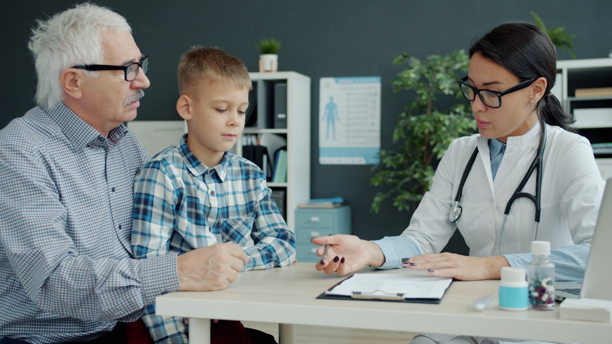 A family physician reviewing care options with an older man and a young boy in her office