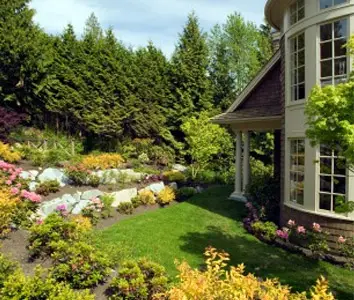 Lush backyard garden with a natural stone wall, manicured lawn, and layered perennial beds