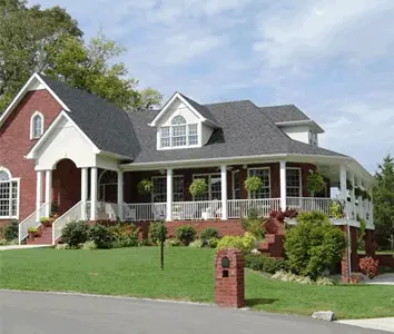 Brick home with a wraparound porch, healthy lawn, and a planted brick mailbox