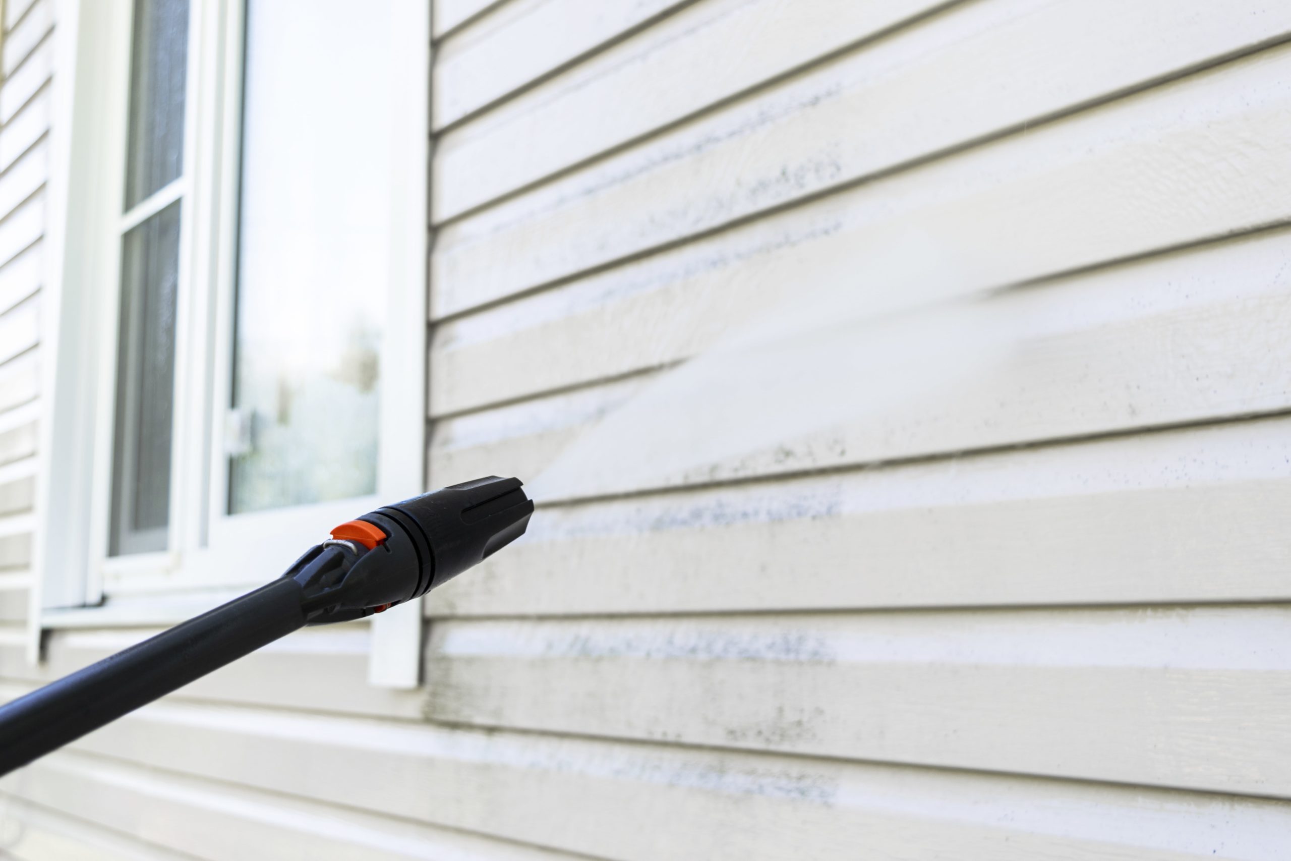 Pressure washing a home exterior to remove dirt and algae