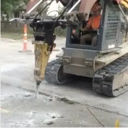 Excavator digging a trench to expose an underground pipe on a job site